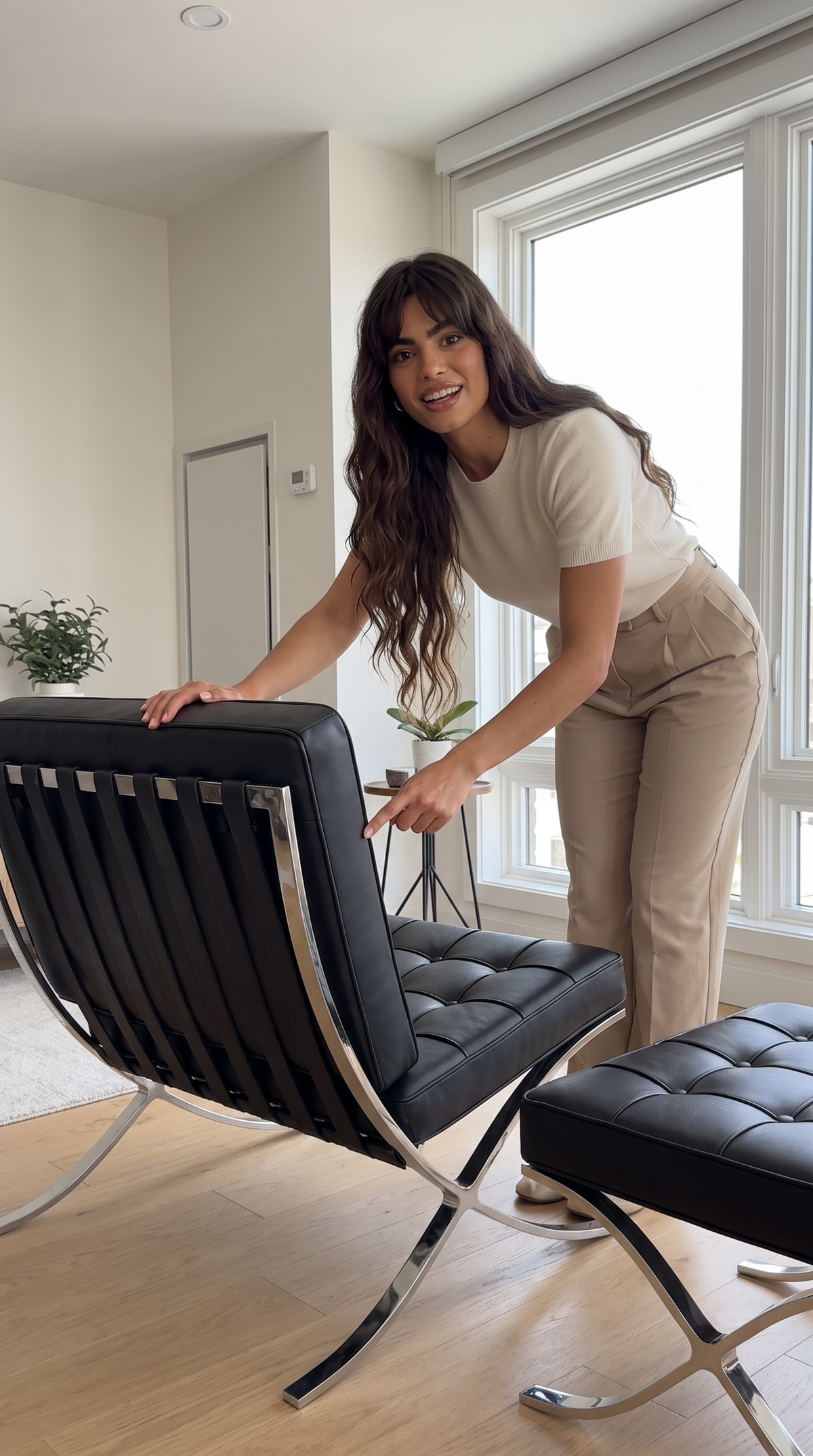 A woman in a beige t-shirt and khaki pants leans over a black leather modern armchair with a matching ottoman