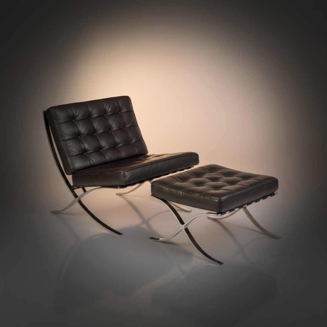 A modern black leather lounge chair with a matching tufted ottoman, both supported by curved chrome metal legs