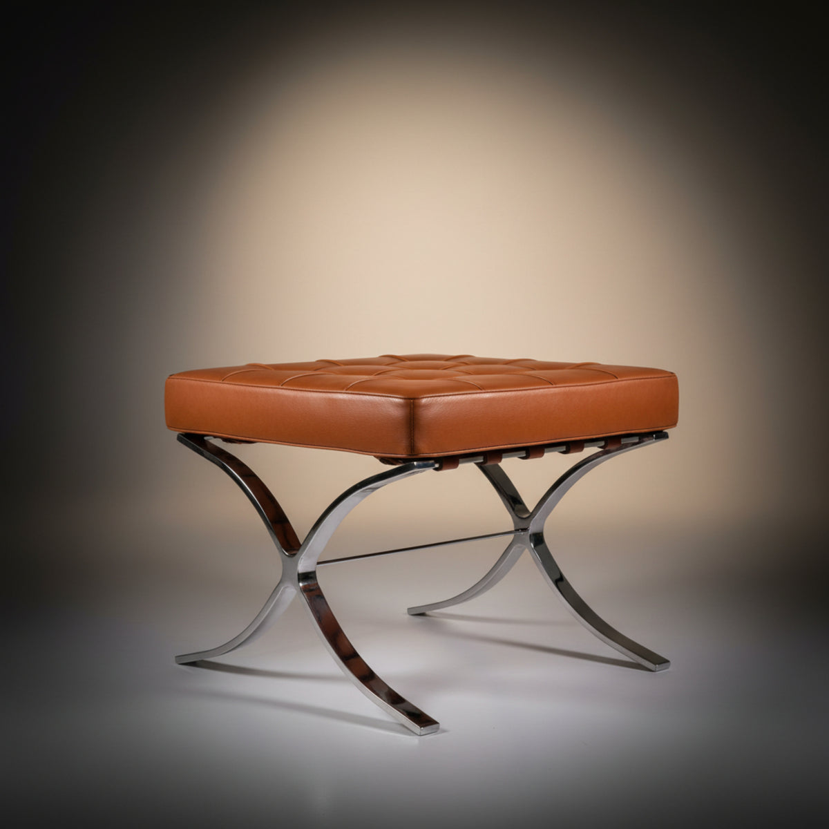 A modern leather bench with a tufted square cushion in warm cognac brown, supported by a polished chrome X-frame base