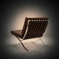A modern brown leather lounge chair with a chrome slatted backrest and curved metal legs, shown from a three-quarters angle 