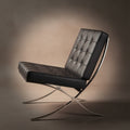 A modern leather lounge chair with a tufted black seat and backrest, supported by a curved polished metal frame